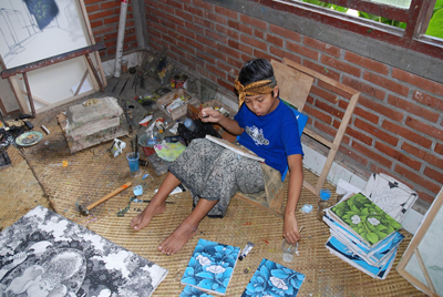 Youn child seated againsta  brick wall.  Child is painting blue and green floral scenes.