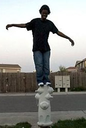 Boy balancing on a fire hydrant with arms outstretched.